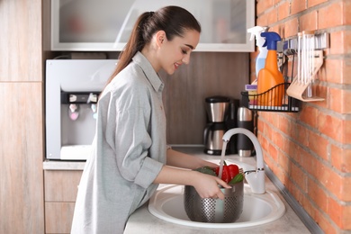 Young woman washing vegetables in kitchen