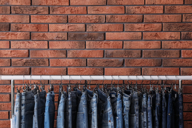 Photo of Rack with stylish jeans near brick wall, closeup. Space for text