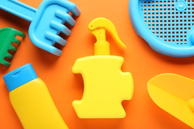 Photo of Bottles of suntan cream and children's beach toys on orange background, flat lay