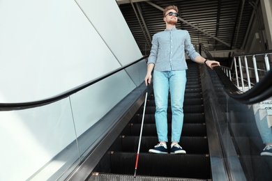 Photo of Blind person with long cane on escalator indoors. Space for text