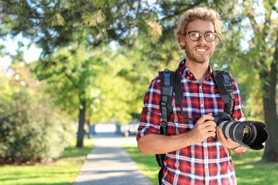 Young male photographer with professional camera in park. Space for text