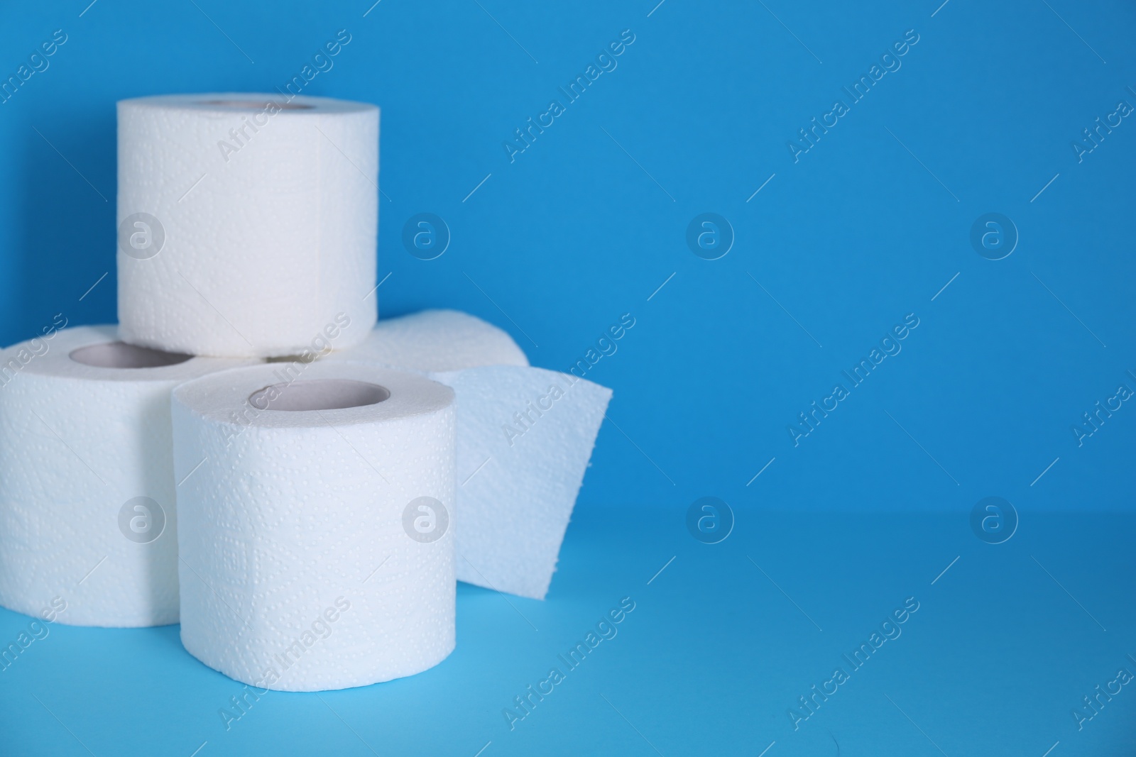 Photo of Soft toilet paper rolls on light blue background. Space for text