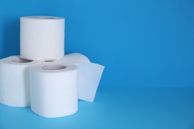 Photo of Soft toilet paper rolls on light blue background. Space for text