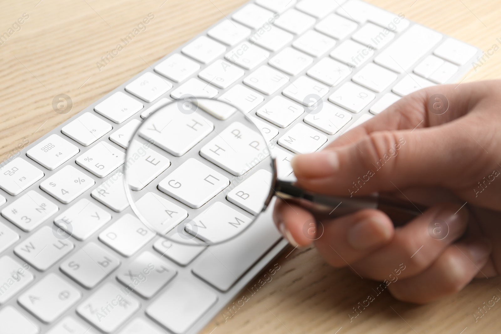 Photo of Woman looking through magnifying glass at computer keyboard on table, closeup. Search concept