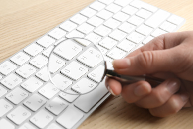 Photo of Woman looking through magnifying glass at computer keyboard on table, closeup. Search concept