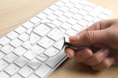 Woman looking through magnifying glass at computer keyboard on table, closeup. Search concept