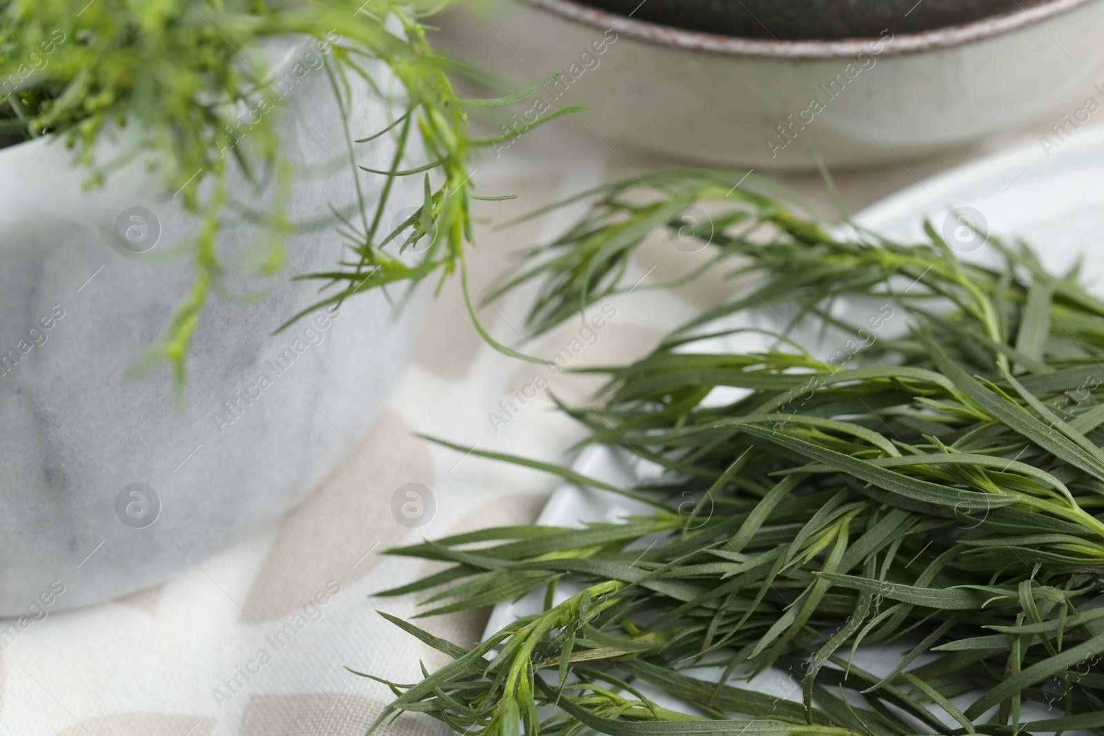 Photo of Plate and mortar with fresh tarragon leaves on table, closeup