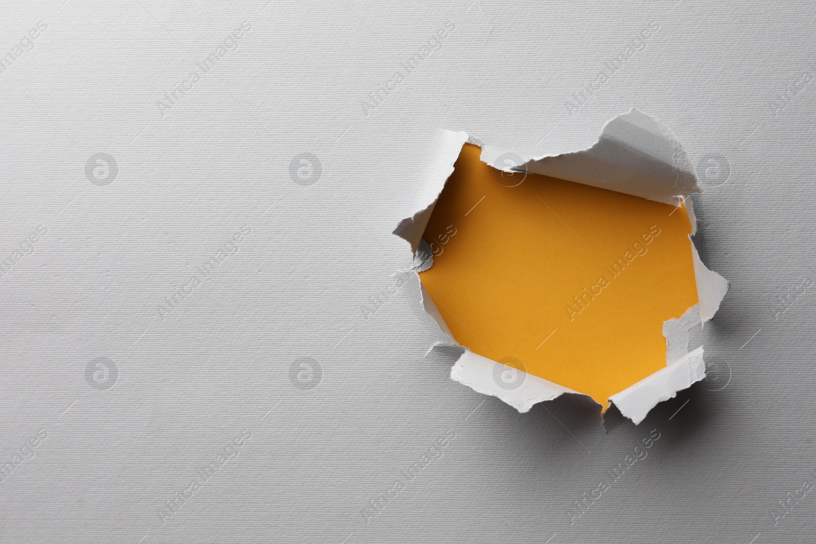 Photo of Hole in white paper on yellow background, space for text