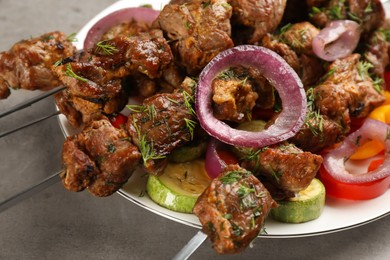 Metal skewers with delicious meat and vegetables served on grey table, closeup