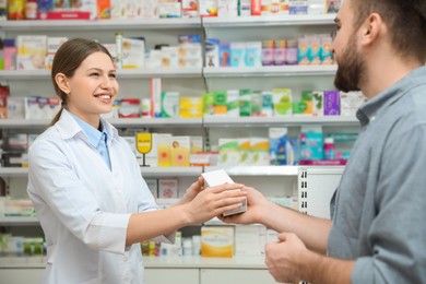 Photo of Professional pharmacist giving medicine to customer in modern drugstore