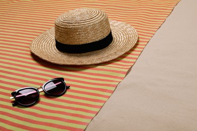 Striped beach towel, hat and sunglasses on sand. Space for text