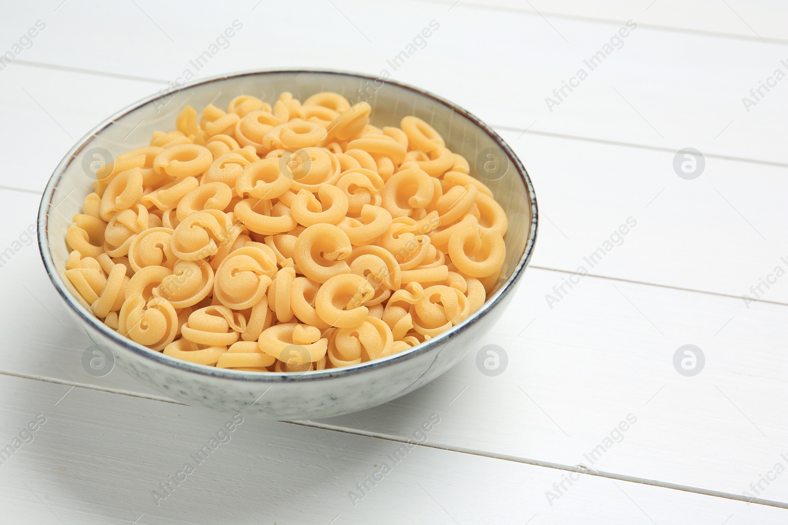 Photo of Raw dischi volanti pasta in bowl on white wooden table, closeup