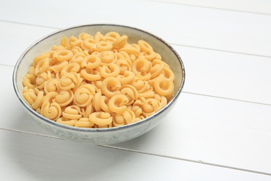 Raw dischi volanti pasta in bowl on white wooden table, closeup