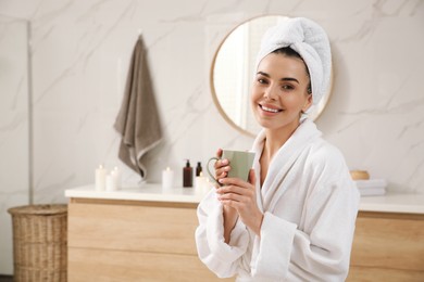 Beautiful young woman with cup of hot drink in bathroom