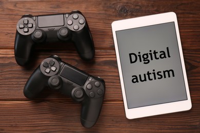 Photo of Tablet with phrase Digital Autism and gamepads on wooden table, flat lay. Addictive behavior