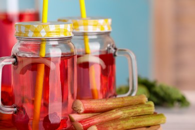 Photo of Mason jars of tasty rhubarb cocktail with raspberry and stalks on table, closeup. Space for text