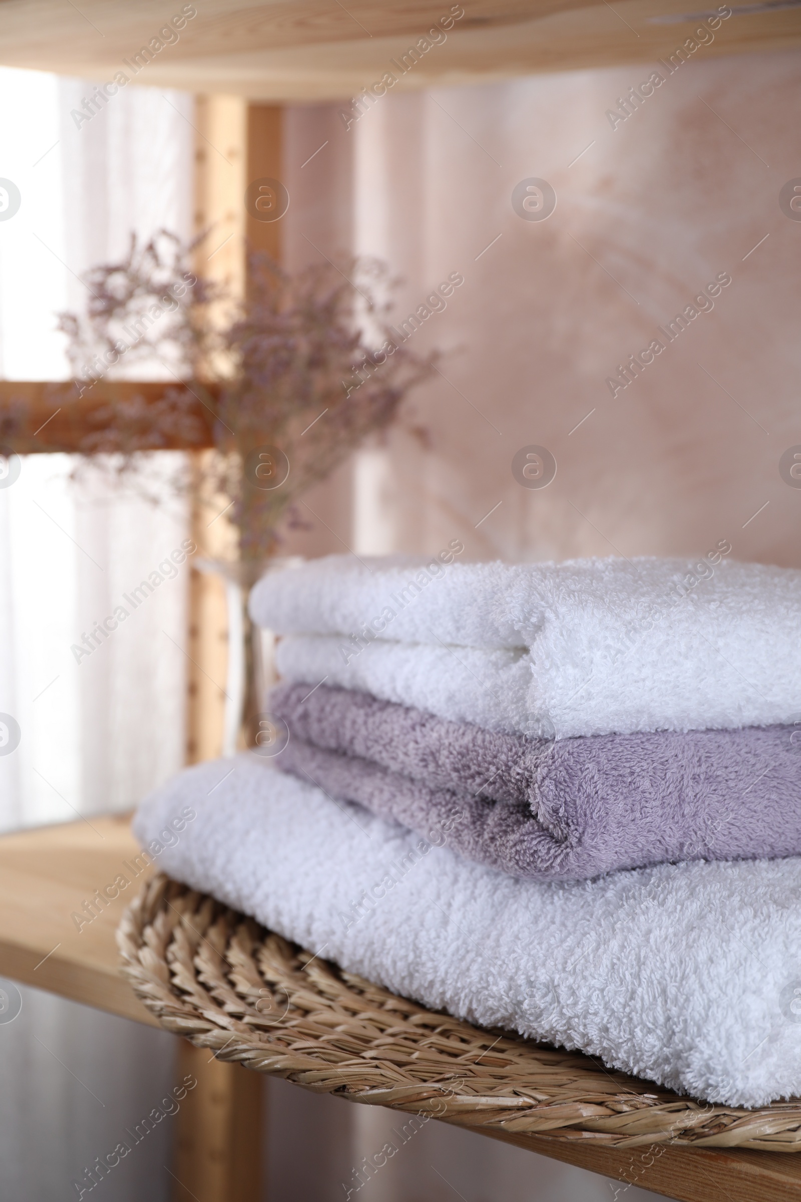 Photo of Stacked soft towels and flowers on shelf indoors