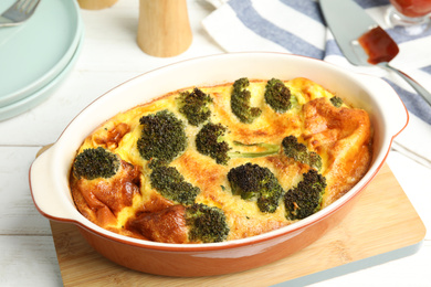 Photo of Tasty broccoli casserole in baking dish on white wooden table