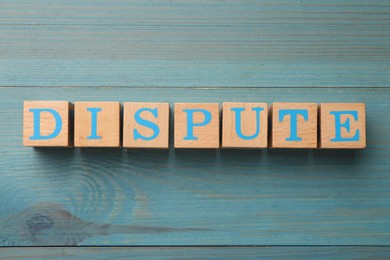 Cubes with word Dispute on light blue wooden table, top view