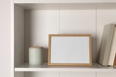 Photo of Empty square frame, candle and books on shelf indoors