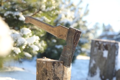 Photo of Metal axe in wooden log outdoors on sunny winter day, closeup