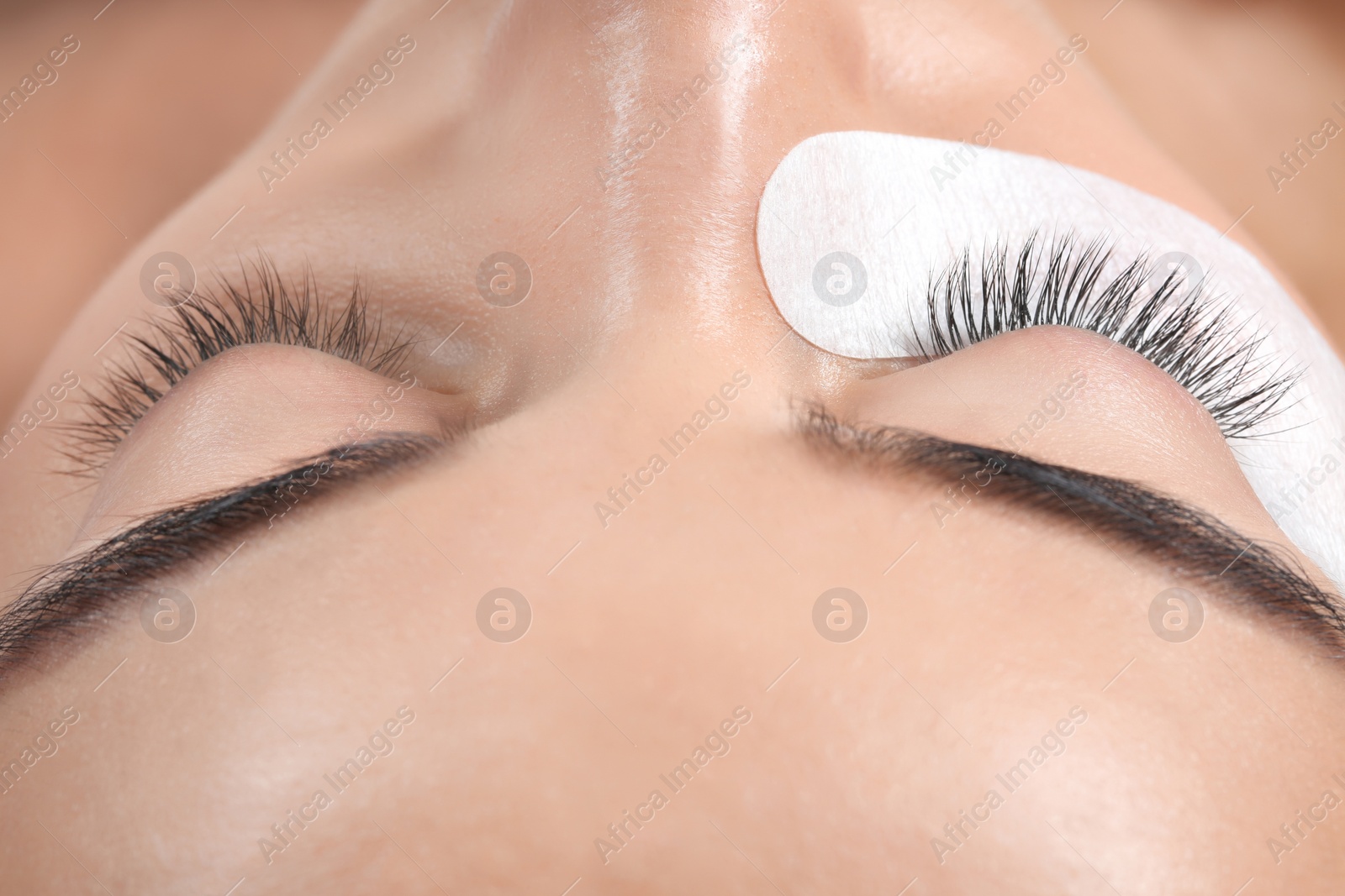 Photo of Young woman undergoing eyelashes extensions procedure, closeup