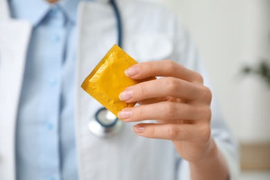 Photo of Female doctor holding condom indoors, closeup. Safe sex concept