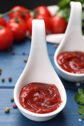 Photo of Organic ketchup in spoons and spices on blue wooden table, closeup. Tomato sauce