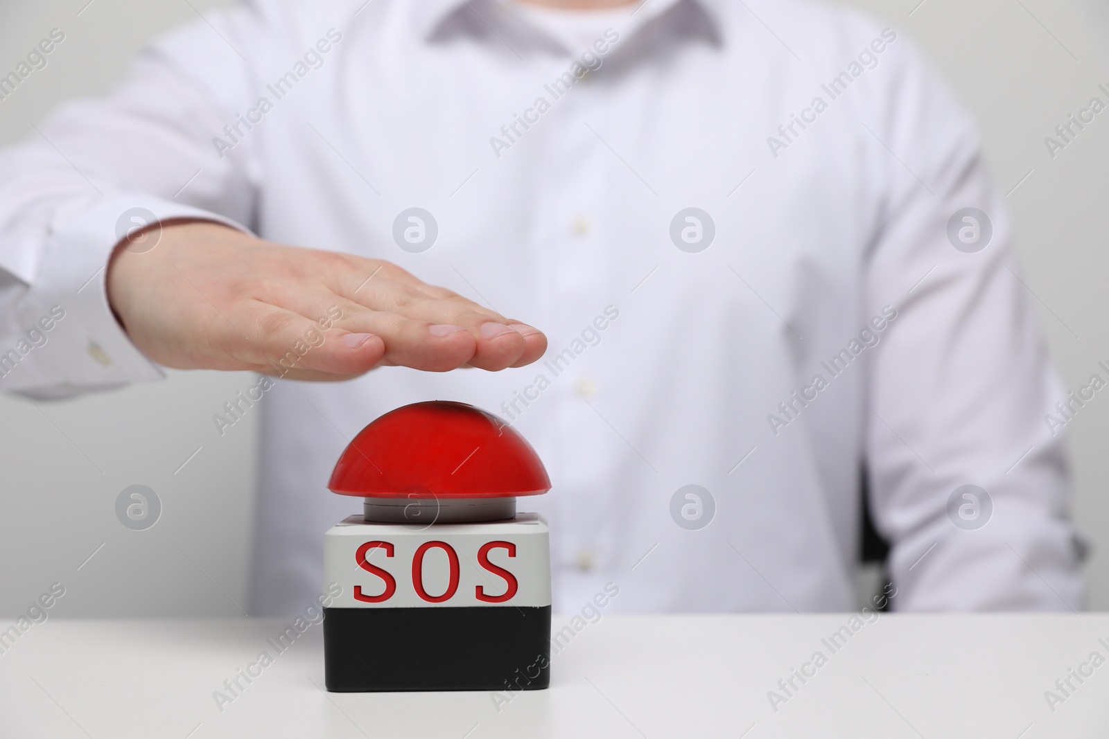 Image of Man pressing red SOS button at white table, closeup