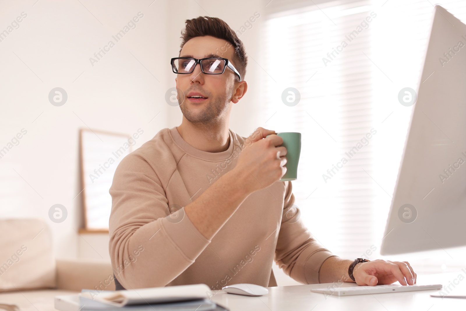 Photo of Young man with cup of drink relaxing at table in office during break