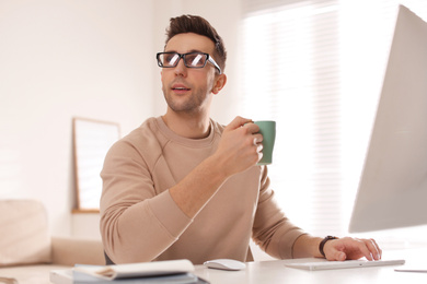 Young man with cup of drink relaxing at table in office during break