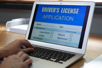Photo of Woman using laptop to fill driver's license application form at table in office, closeup