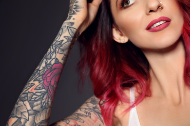 Photo of Beautiful woman with tattoos on arm against black background, closeup