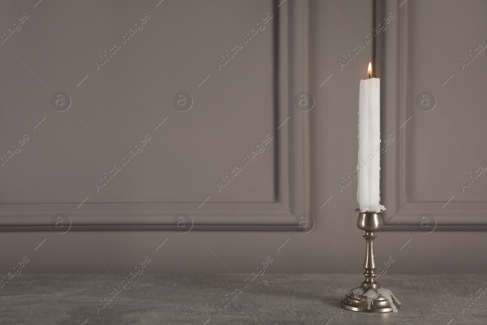 Photo of Elegant candlestick with burning candle on grey table. Space for text