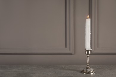 Photo of Elegant candlestick with burning candle on grey table. Space for text