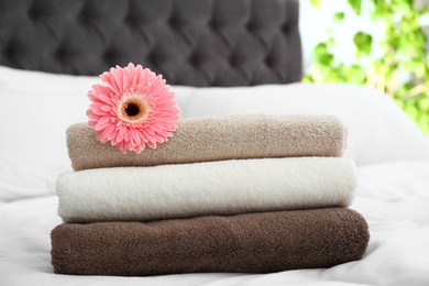 Stack of clean towels and beautiful gerbera flower on bed