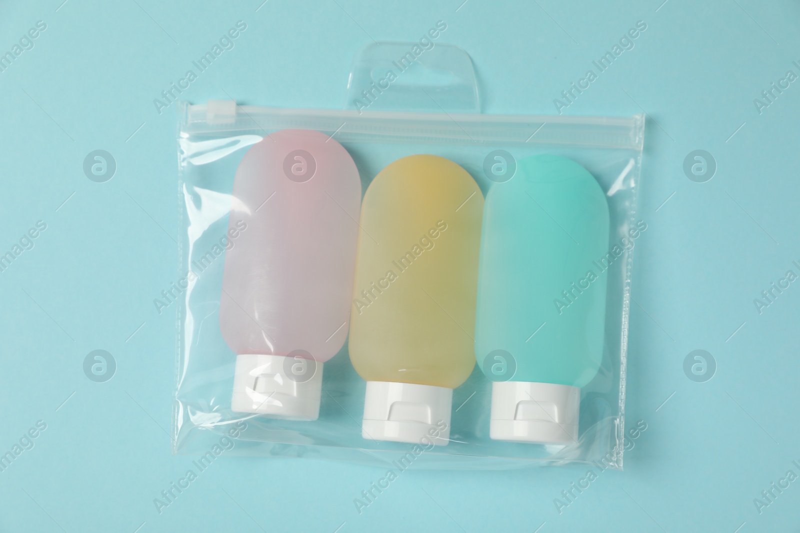 Photo of Cosmetic travel kit in plastic bag on light blue background, top view. Bath accessories