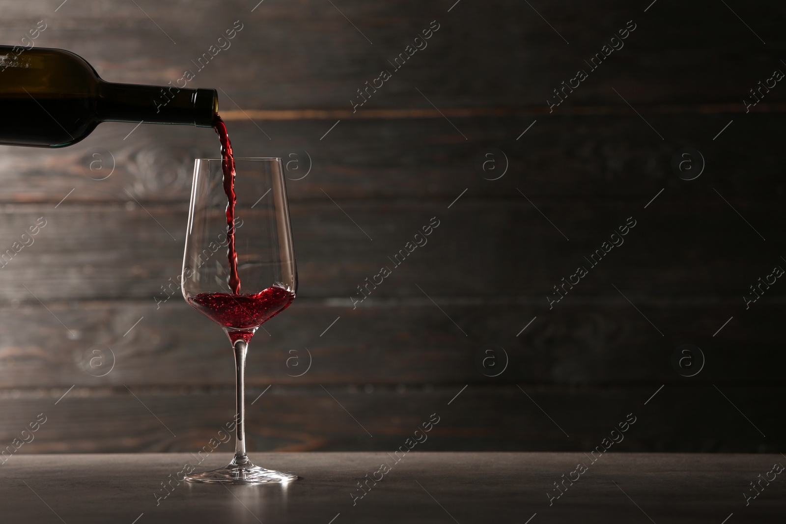 Photo of Pouring red wine into glass from bottle on table against wooden background. Space for text