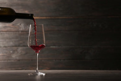 Photo of Pouring red wine into glass from bottle on table against wooden background. Space for text