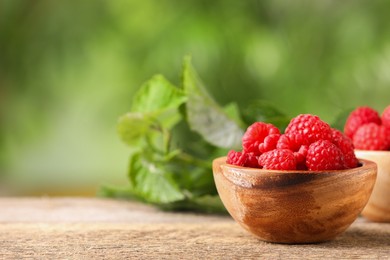 Photo of Tasty ripe raspberries in bowl on wooden table outdoors. Space for text
