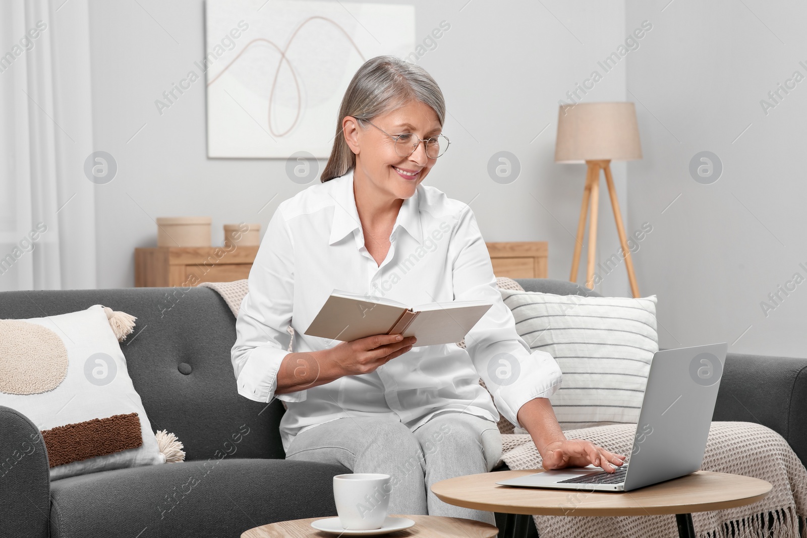 Photo of Beautiful senior woman with notebook using laptop at home