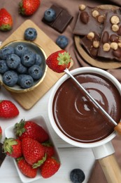 Photo of Fondue pot with chocolate, different berries and fork on white wooden table, flat lay