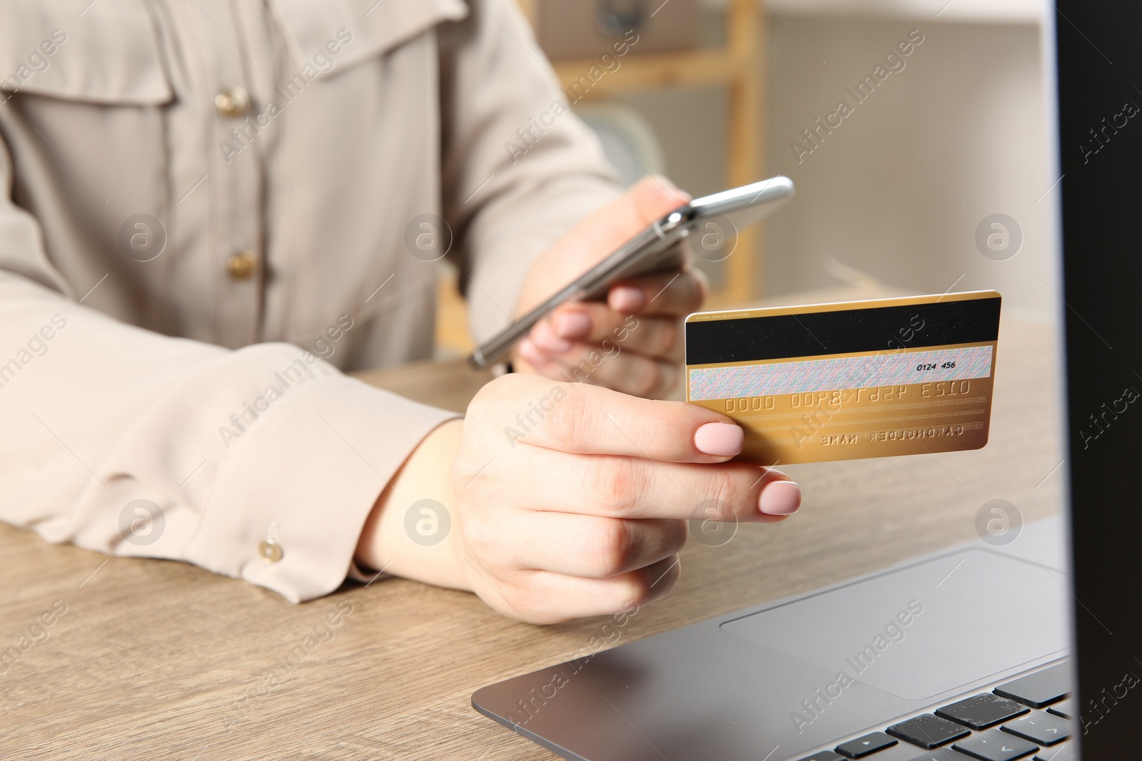 Photo of Online payment. Woman using smartphone and credit card near laptop at wooden table indoors, closeup