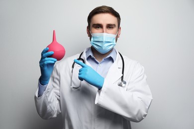 Photo of Doctor holding rubber enema on grey background
