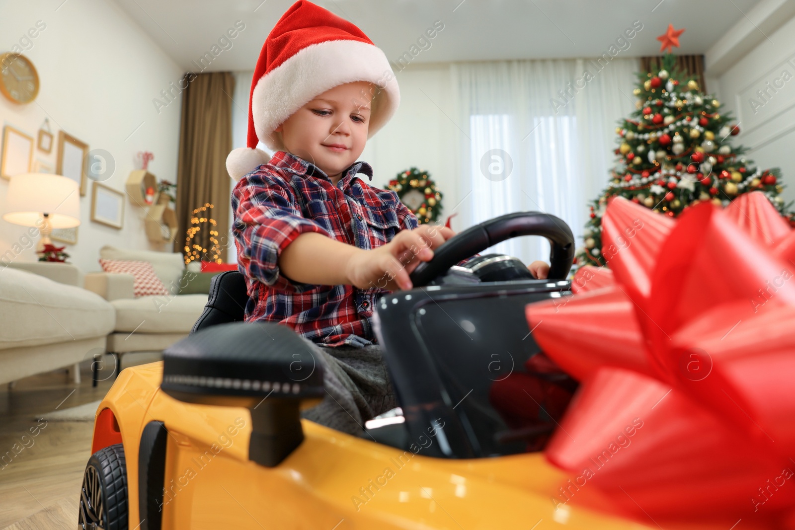 Photo of Cute little boy driving toy car in room decorated for Christmas