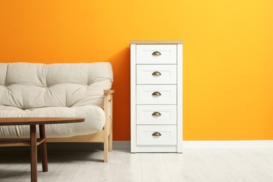 Photo of Stylish beige sofa, chest of drawers and wooden coffee table near orange wall indoors. Interior design