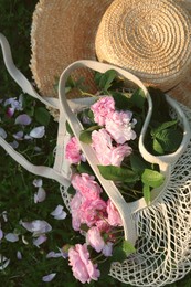 Photo of Straw hat and mesh bag with beautiful tea roses on green grass outdoors