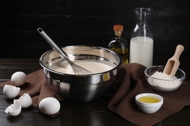 Composition with whisk and dough in bowl on dark wooden table