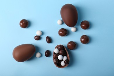 Photo of Tasty chocolate eggs and different sweets on light blue background, flat lay