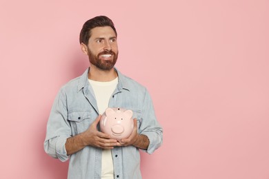 Happy man with ceramic piggy bank on pale pink background, space for text